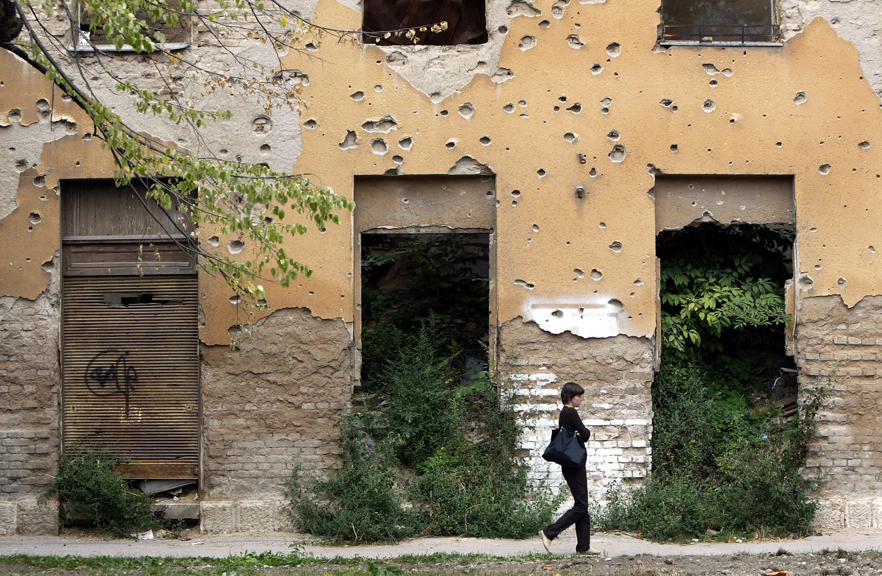 A woman walks past bullet-riddled buildings, remnants of the war. Bosnia and Herzegovina, 2004.