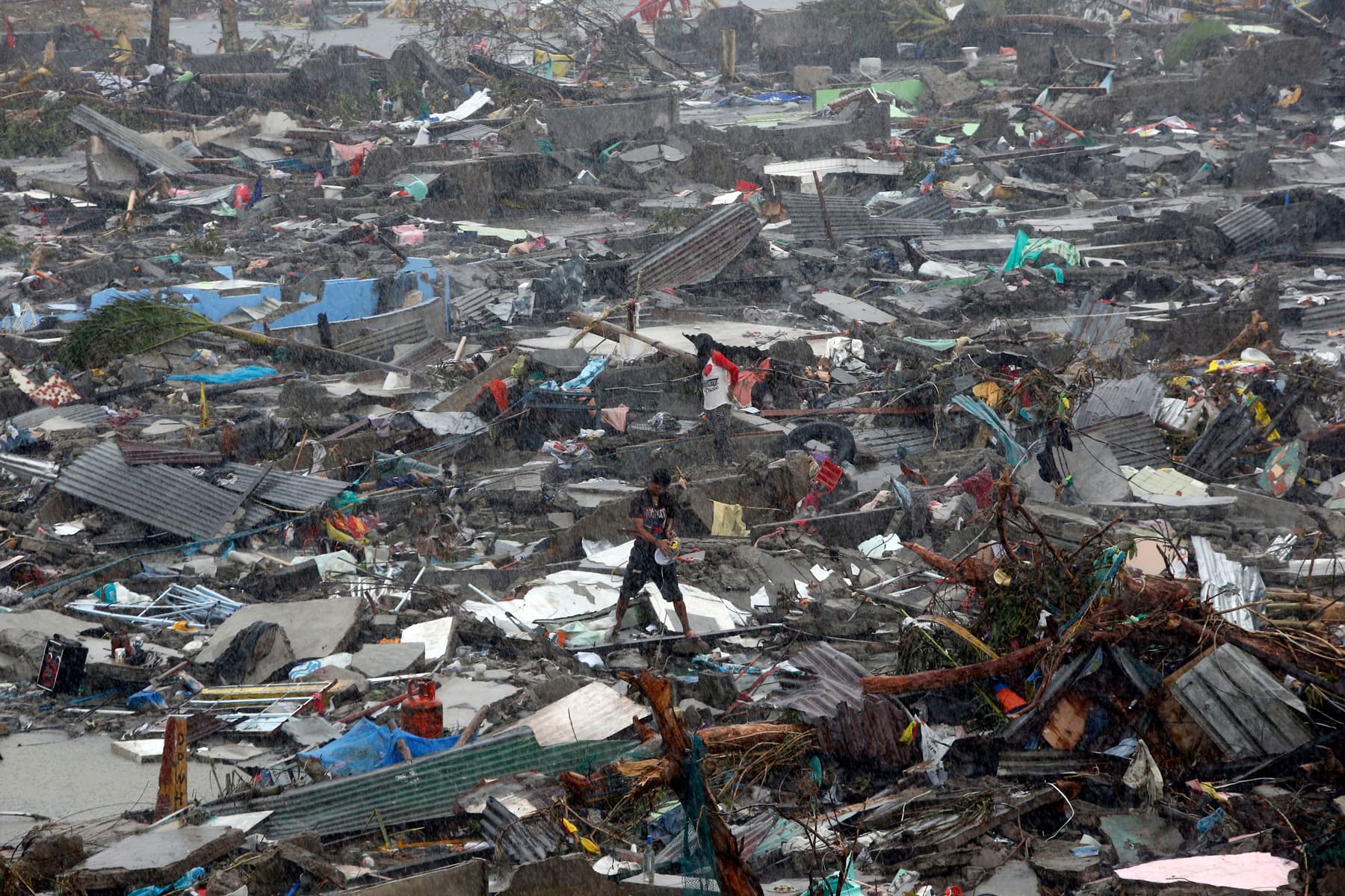 Islamic Relief staff stands atop debris as residents salvage belongings from the ruins of their houses after Typhoon Haiyan battered Tacloban city. Philippines, 2013.