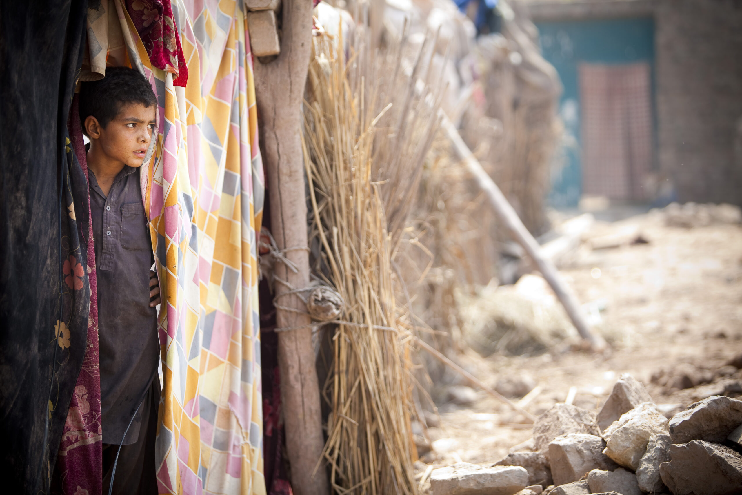 A boy looks out from a shelter made of straw and logs following devastating flooding in Pakistan. Pakistan, 2010.