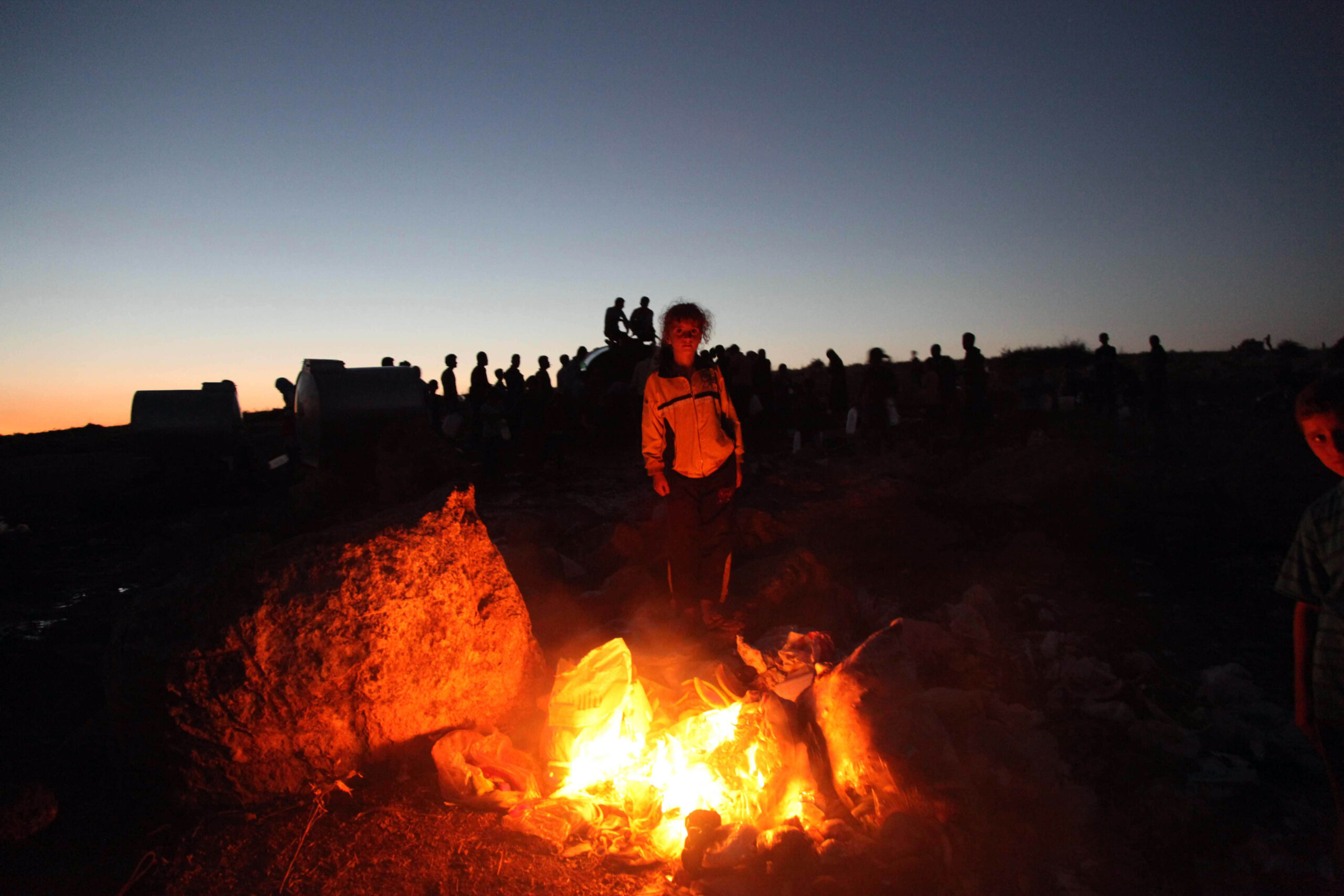A child warms herself by a fire at a camp for displaced people in Syria. Syria, 2012.