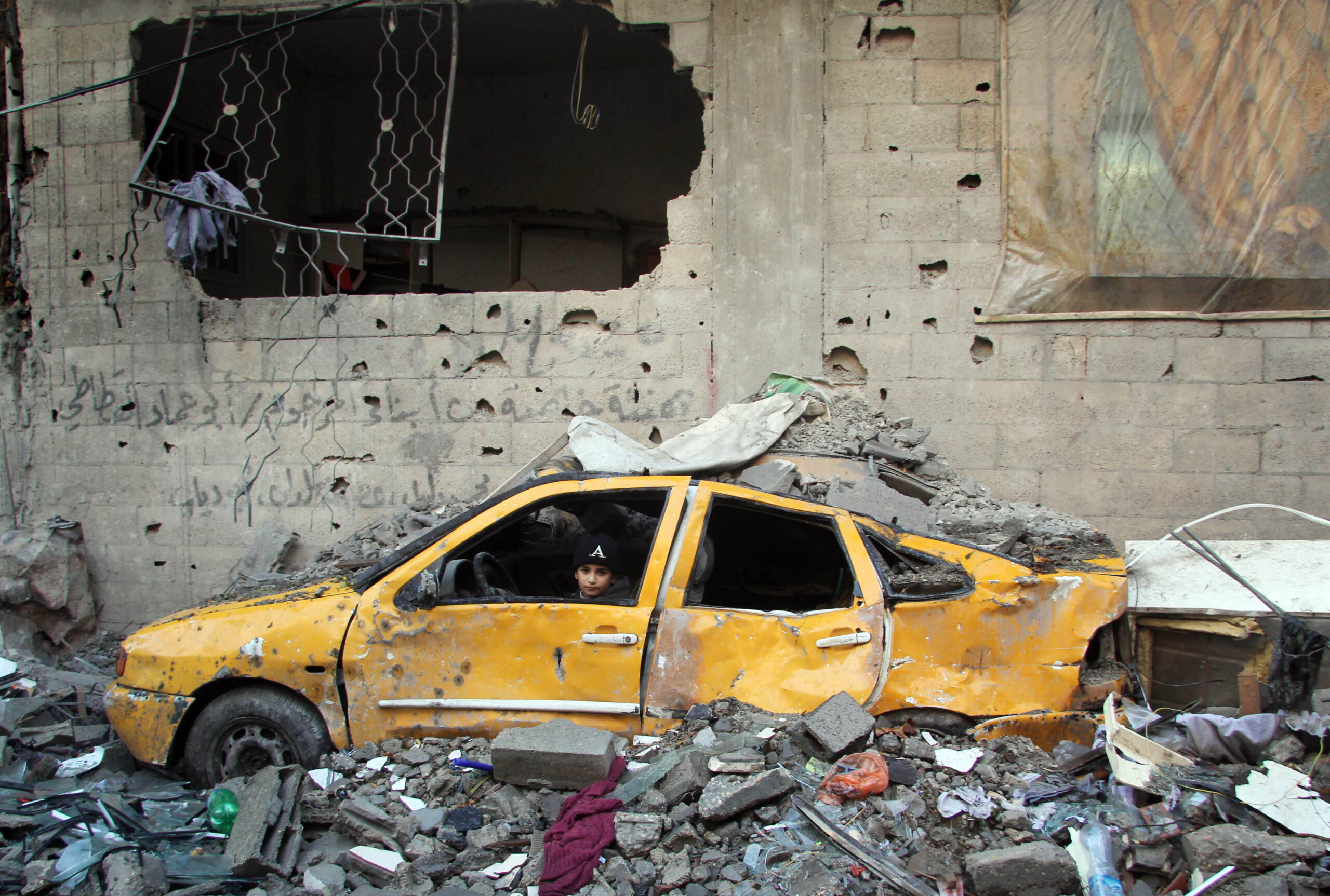 A child sits in a car partly crushed by rubble during an escalation in Gaza. Occupied Palestinian Territory, 2012.
